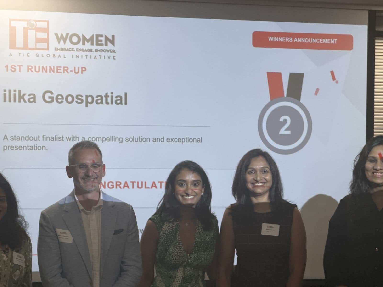 The winners announcement at the TiE Jersey Women Pitch Competition 2026 final, naming Ilika Geospatial as first runner-up
